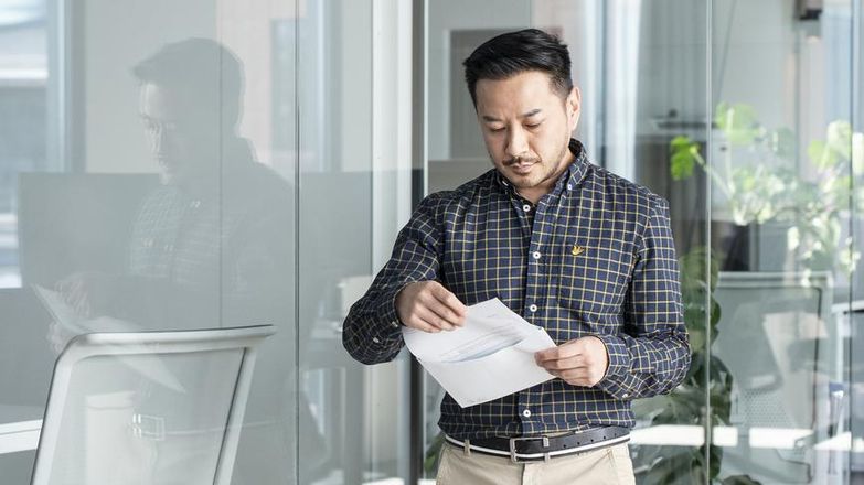 Man staat in een kantoor en haalt een brief uit een envelop.